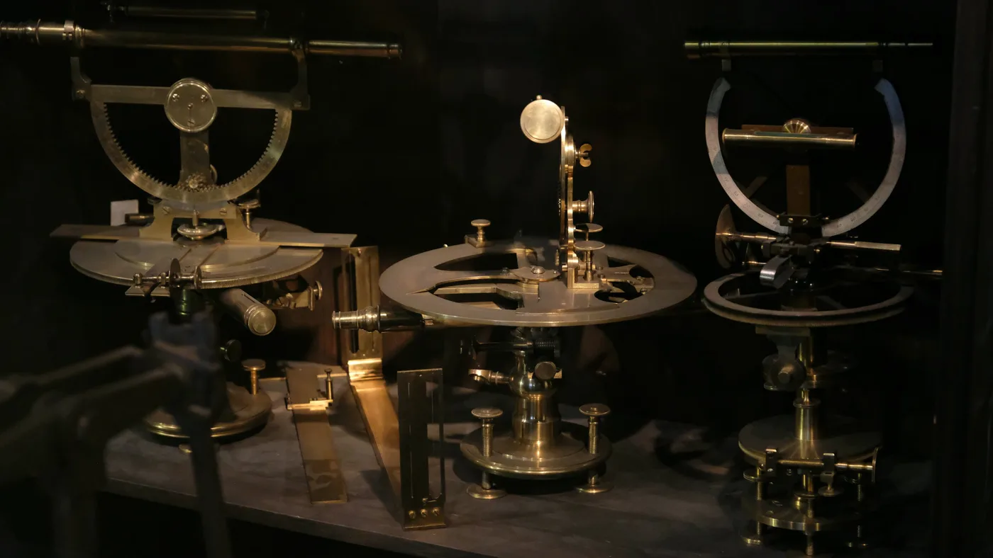 Three antique brass surveying instruments with graduated arc scales on a shelf in near darkness