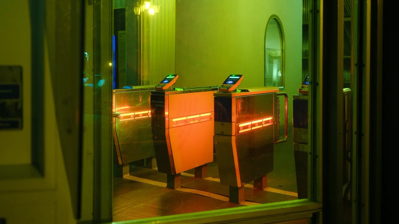 Empty subway turnstiles glowing orange and green at night in a dark, deserted station