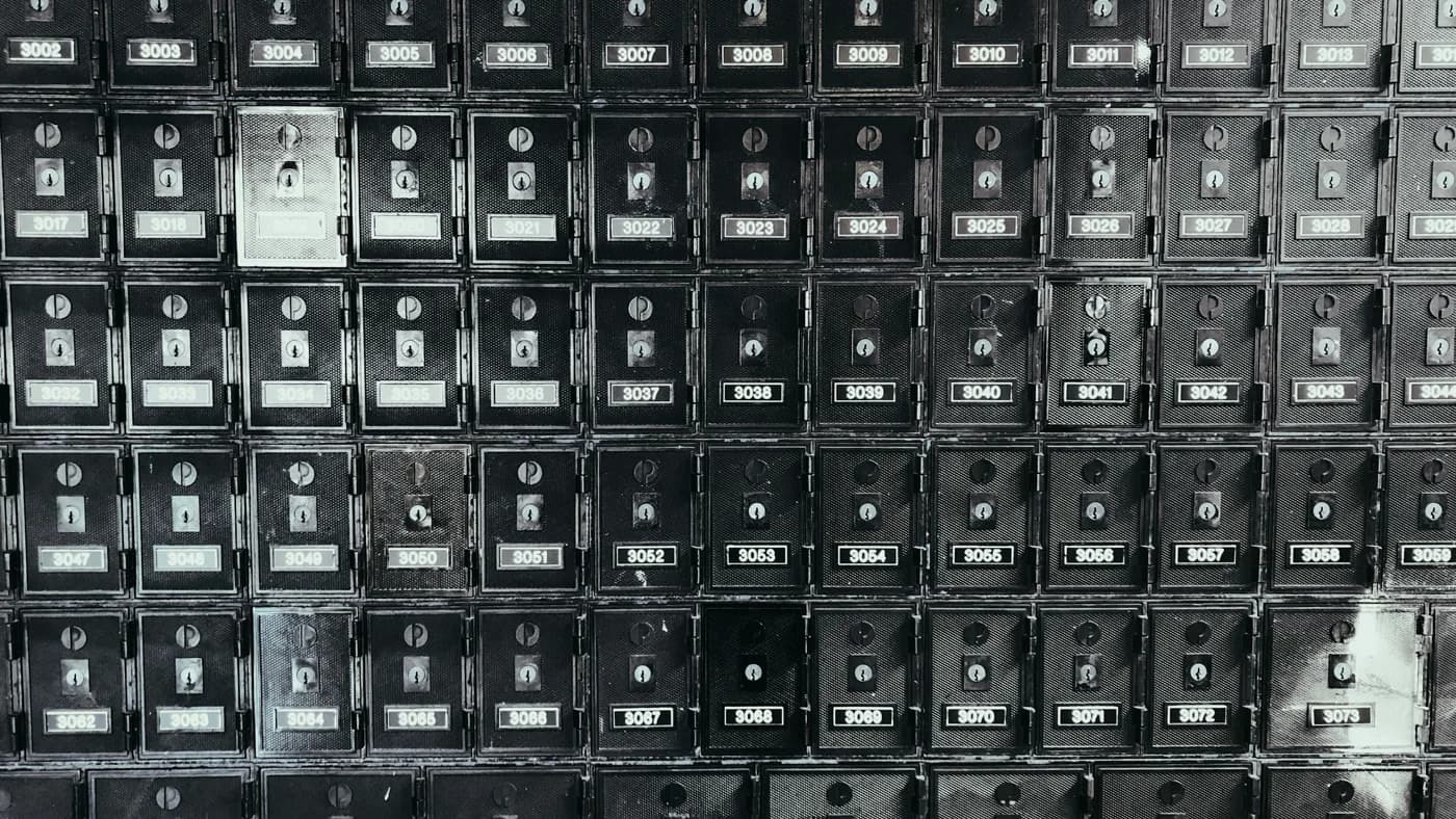 A wall grid of identical dark metal post office box doors with one blank door standing out among them