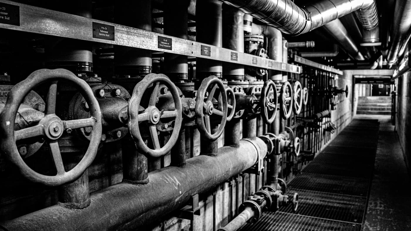 A receding row of cast-iron valve handwheels bolted to a pipe run in a dark corridor