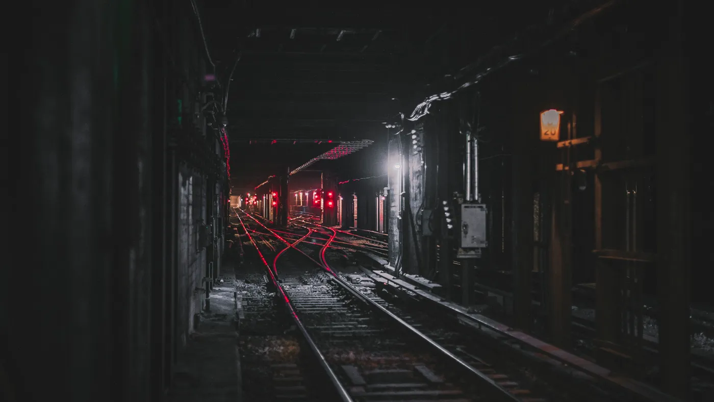 Dark railway tunnel where the tracks split at a junction into several branches, lit red by signal lights