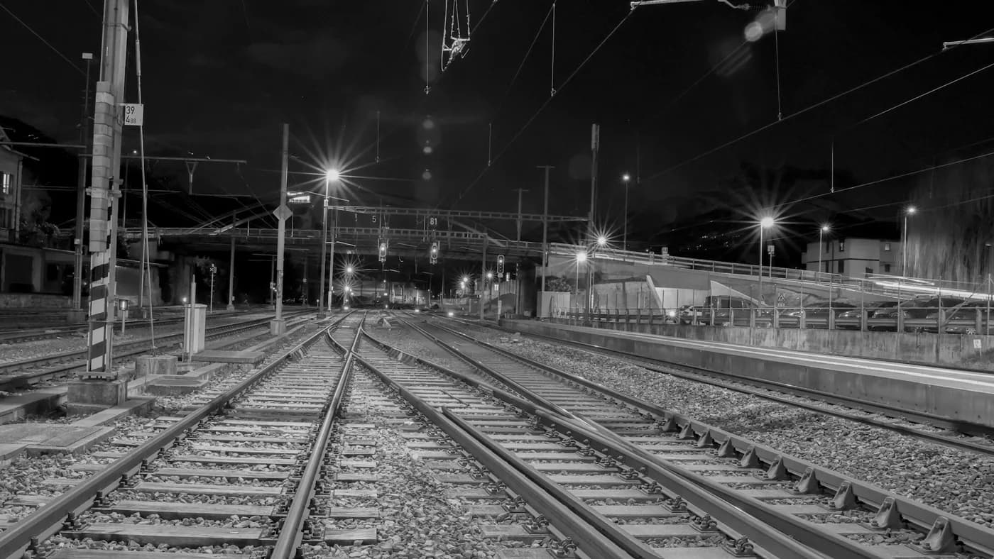Black and white railway tracks diverging at a switch under station lights at night