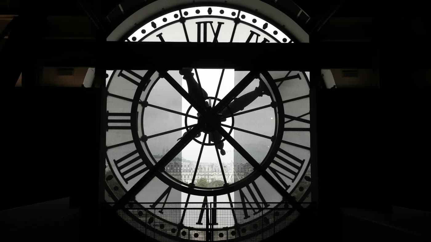 A large illuminated station clock face silhouetted against a city skyline at dusk