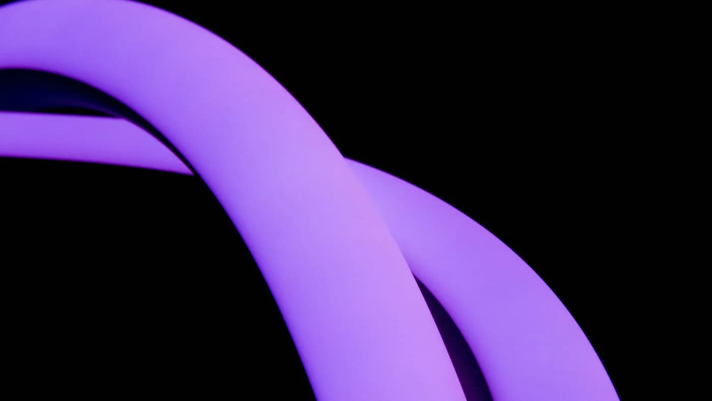 Two curved purple neon tubes glowing and crossing against a solid black background
