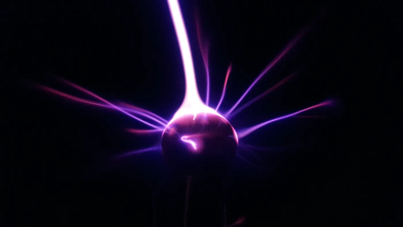 Violet plasma filaments arcing from a glowing electrode inside a plasma ball on black