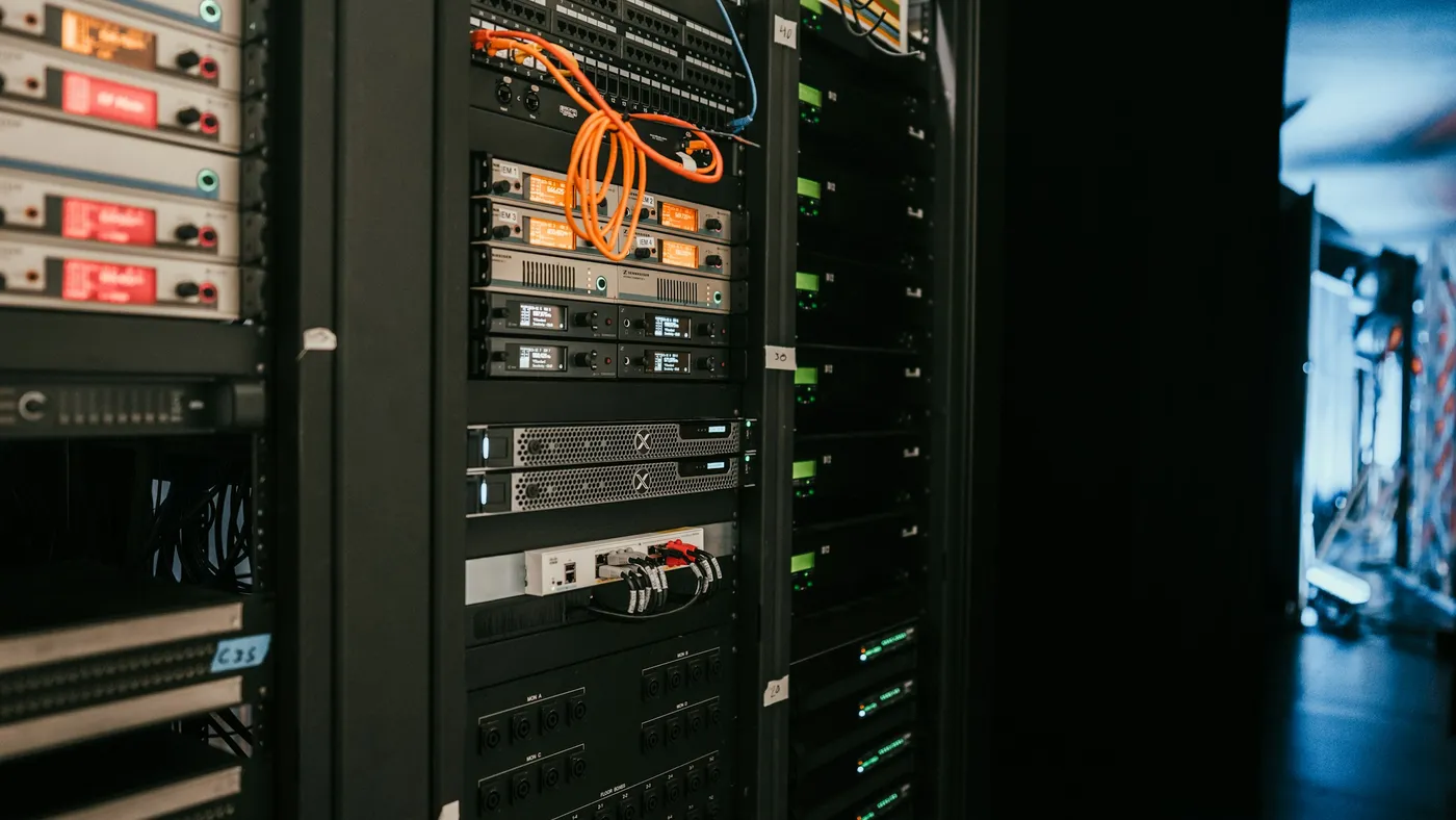 Dark server rack with glowing status displays and a coiled orange network cable hanging from a patch panel
