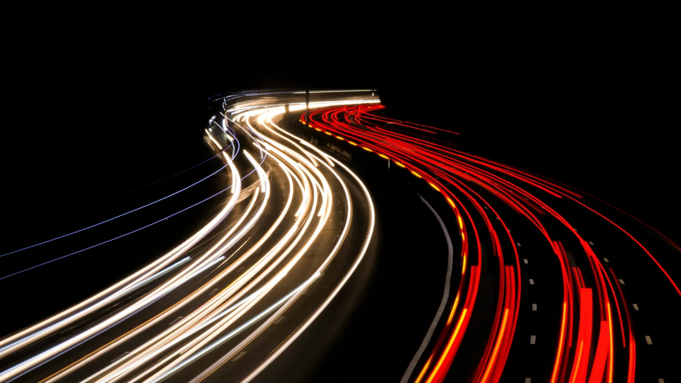 Night highway from above with two separated streams of light trails running toward one point