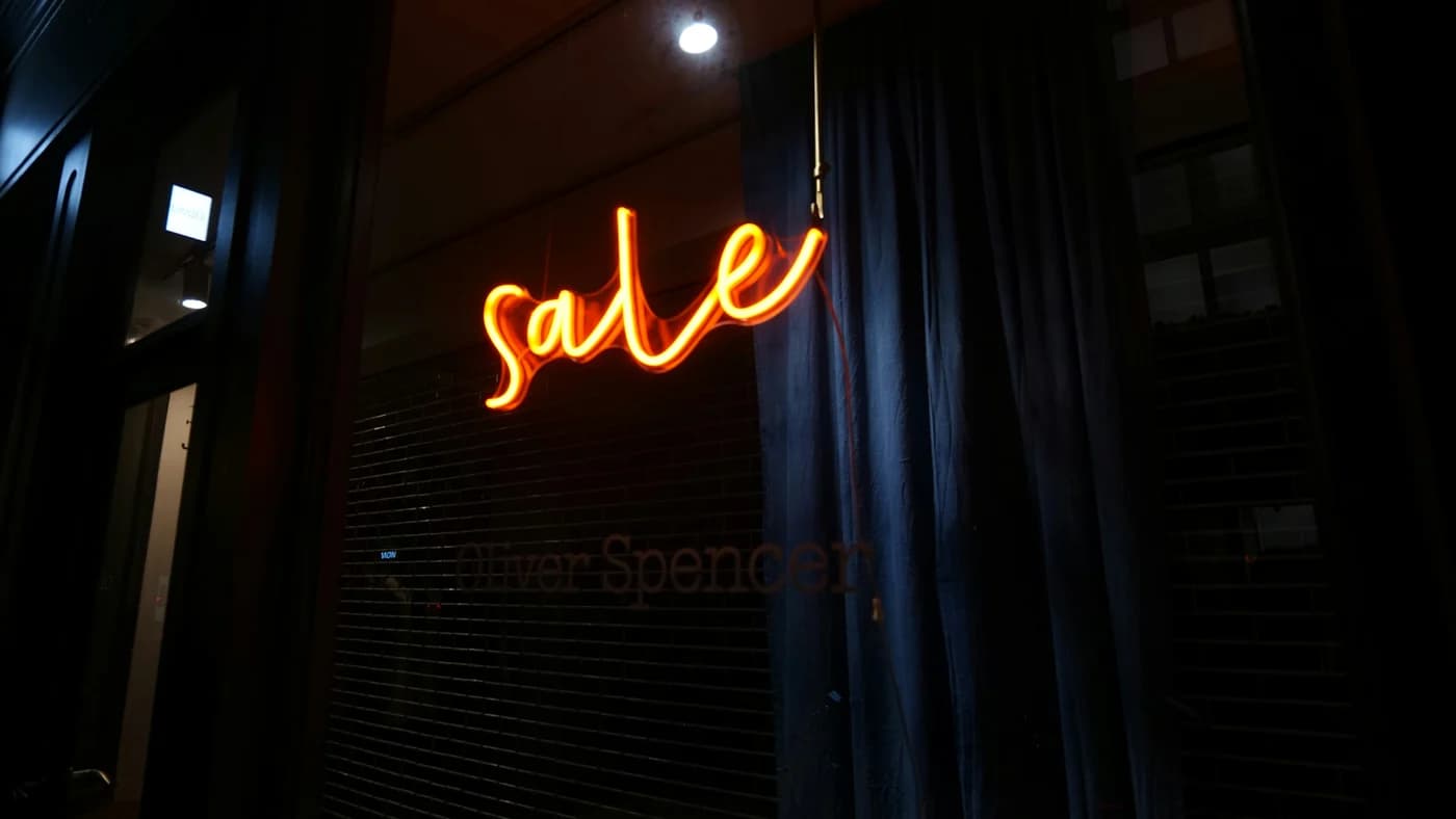 An orange neon sale sign glowing in a dark shop window at night