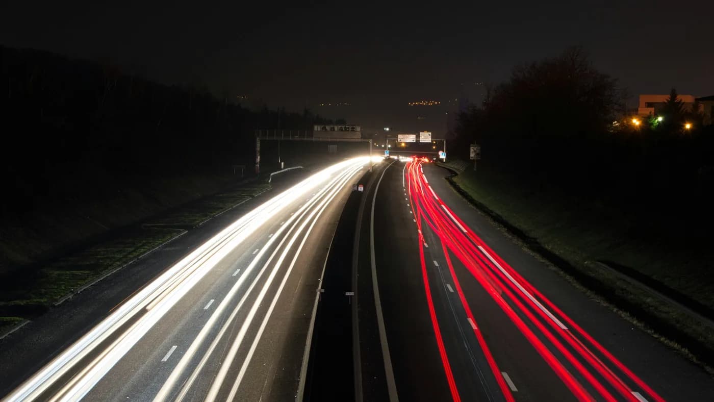 Long-exposure photo of a highway at night, with white headlight trails on the left and red taillight trails on the right