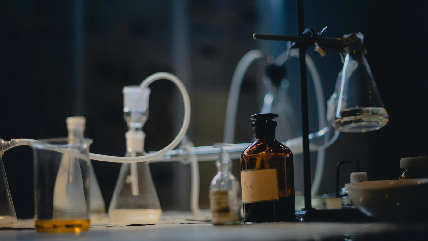 Lab bench in low light with flasks, tubing, an amber reagent bottle and a beaker of orange liquid