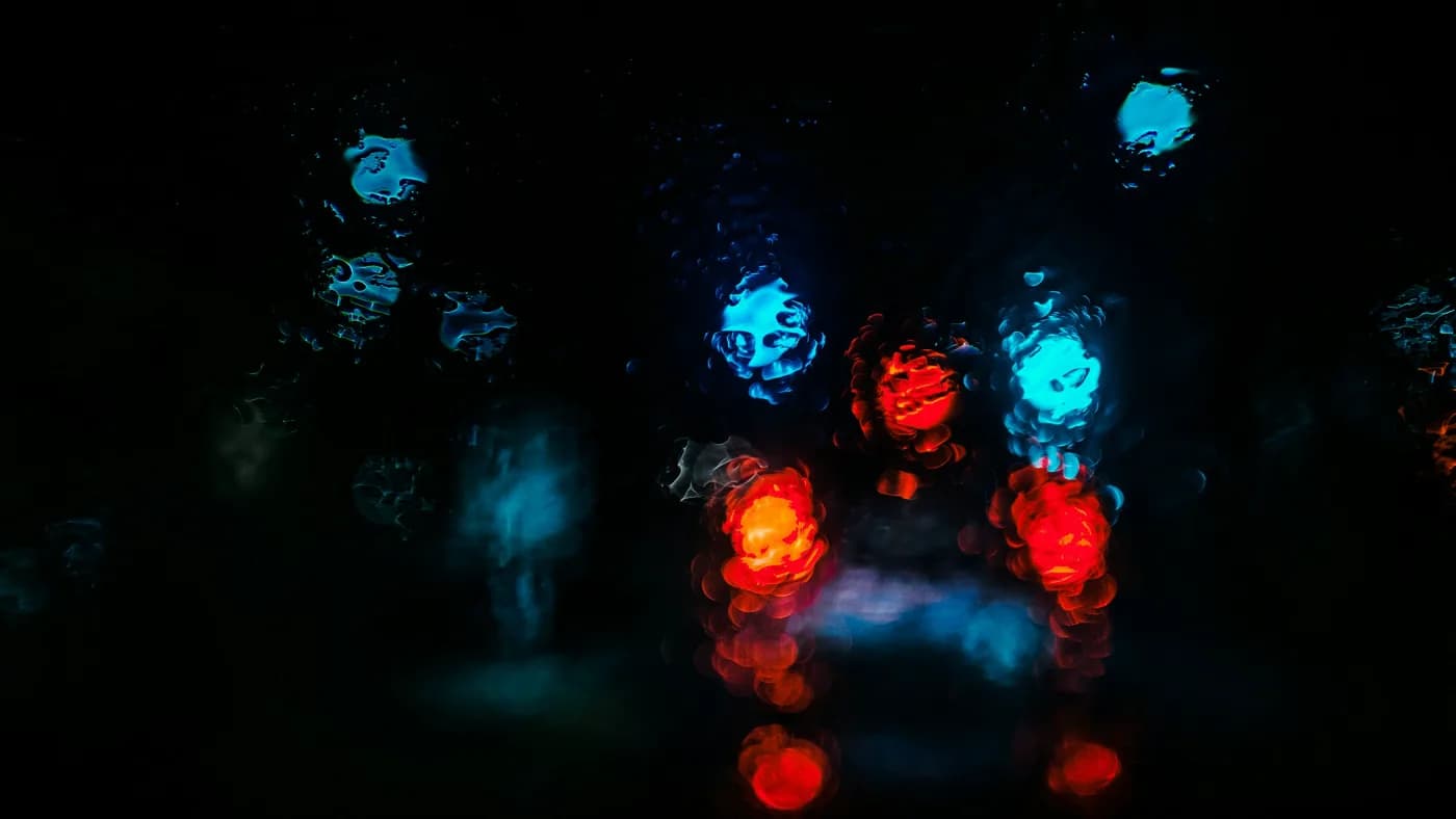 Blurred red and blue lights glowing through rain-streaked glass against a dark background