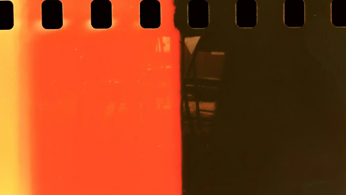 Macro of a film negative with a hard edge where bright orange light leak falls off into black