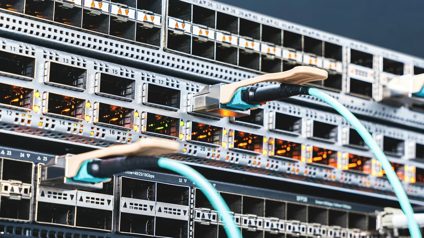 Close-up of a dark network switch with rows of empty ports and two fibre cables plugged in, one glowing orange