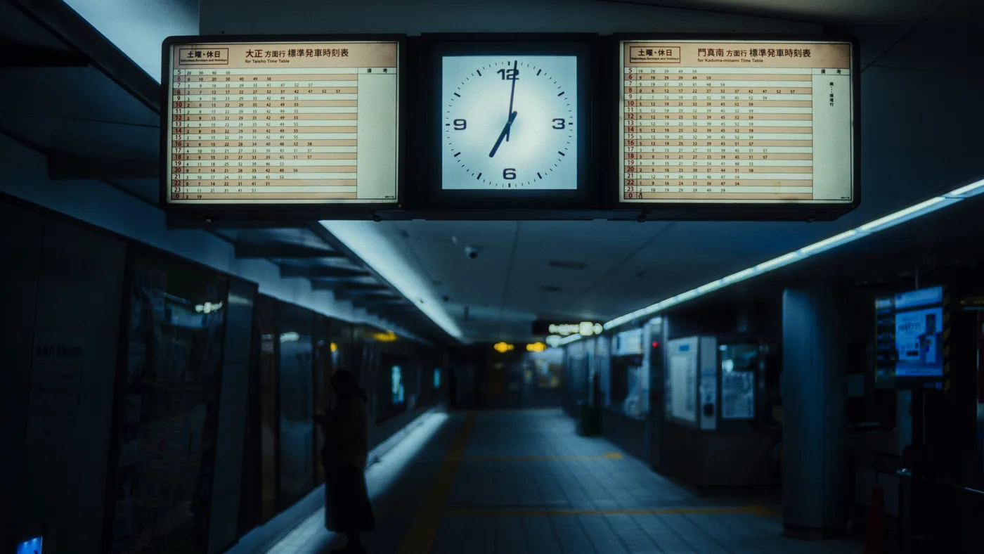 A lit analog station clock and two timetables above a dim, near-empty subway platform
