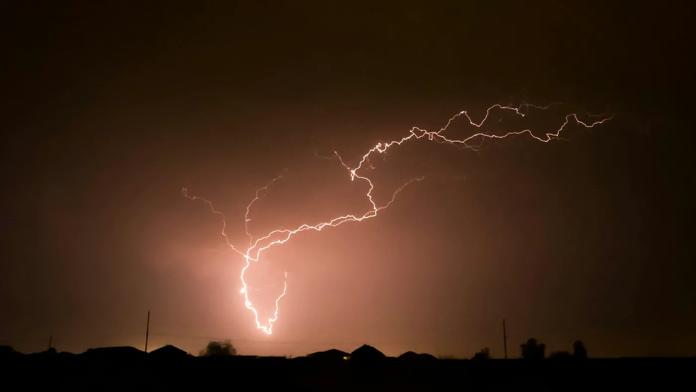 Branching lightning bolt across a dark night sky above silhouetted rooftops and utility poles