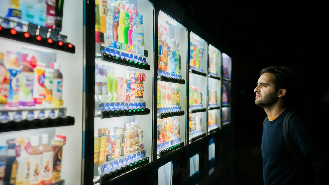 A man stands at night before a row of brightly lit vending machines on a dark Tokyo street