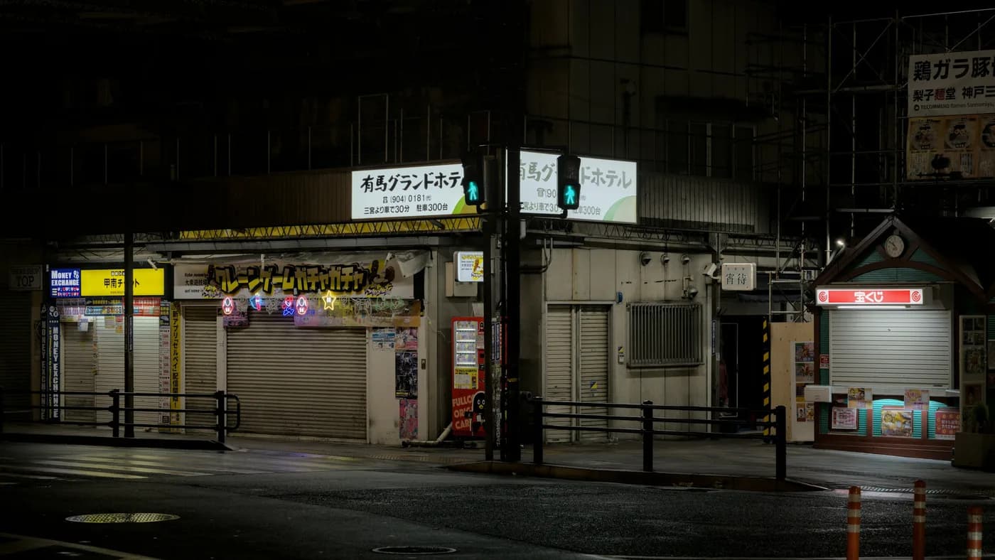Shuttered storefronts at night with lit signboards still glowing above closed metal roller shutters