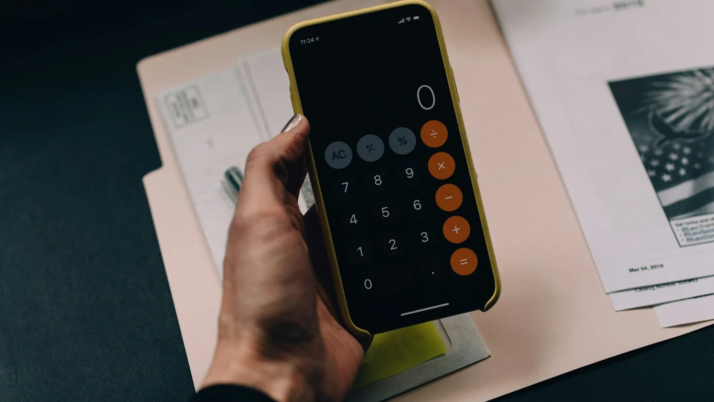 Person reviewing financial documents at a desk with a calculator and laptop