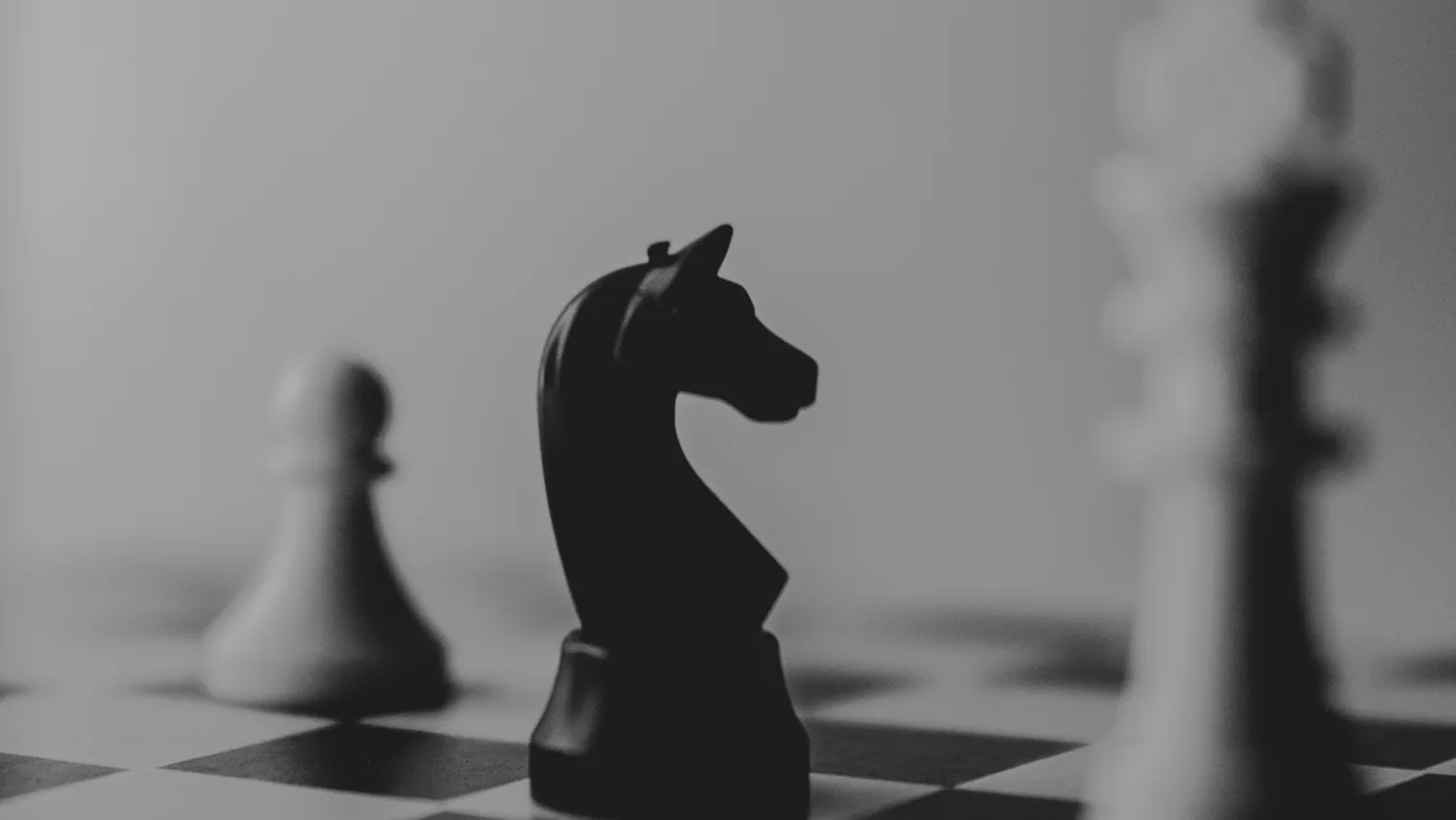 A black knight chess piece facing white pieces across a board