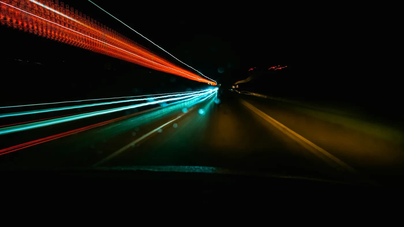 Red and cyan light trails streaking down a dark highway at night, long-exposure motion blur