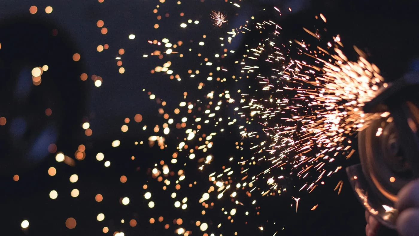 Bright orange sparks fly from a grinder against a dark night background with glowing bokeh lights